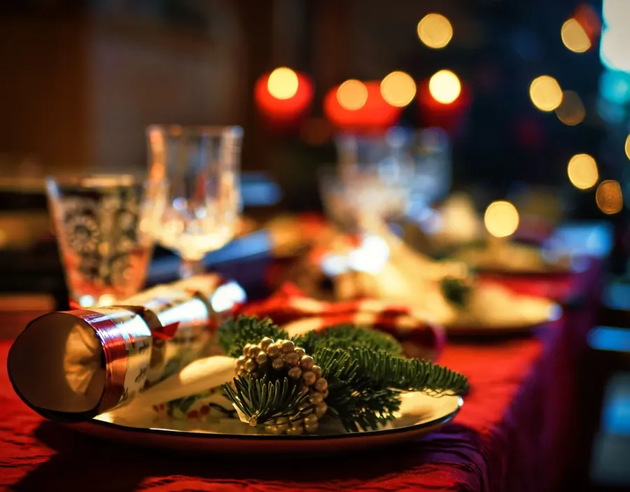 Julefrokostbord dækket med levende lys, gran og røde servietter i varmt lys