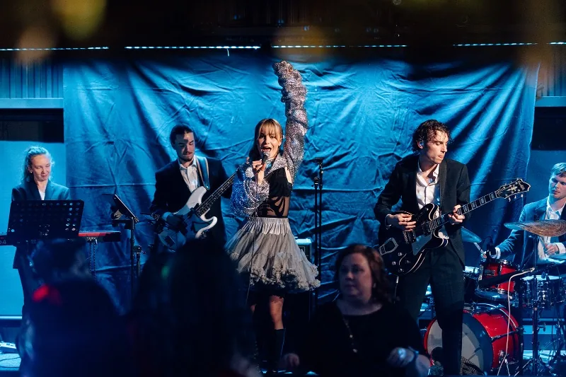 Liveband med sångerska, gitarrister, klaviatur och trummor på en scen i blått ljus