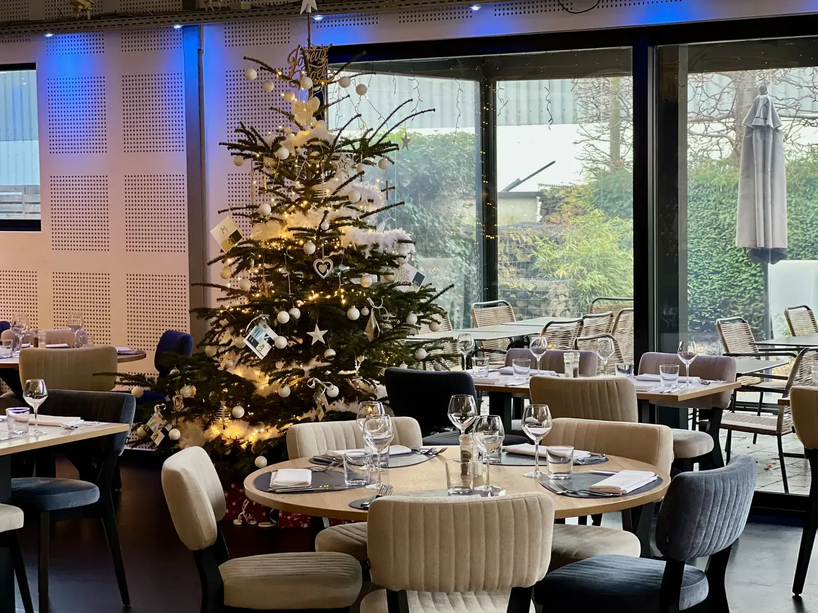 Restaurant med dækkede borde og et juletræ med hvide kugler i vinduet