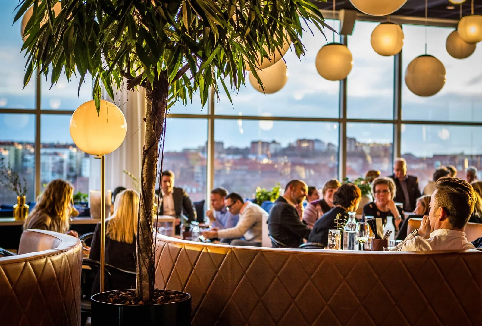 Fullsatt restaurang i kvällsljus med klotlampor och utsikt över staden
