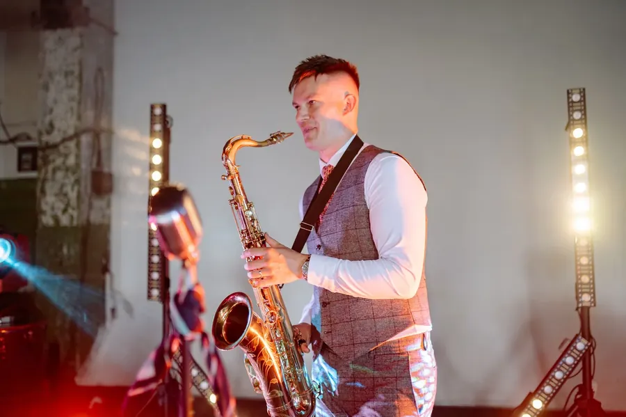 Saxofonist i vest spiller på en scene i varmt lys