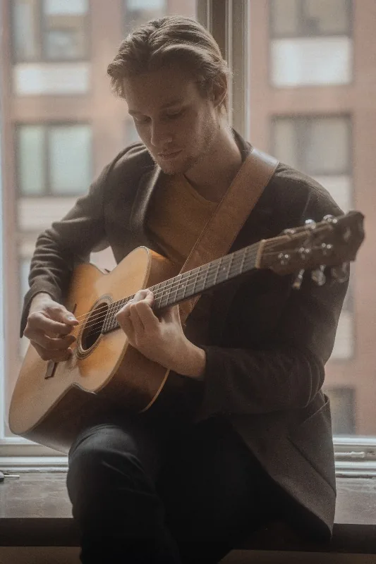 Trubadur spelar akustisk gitarr vid ett fönster