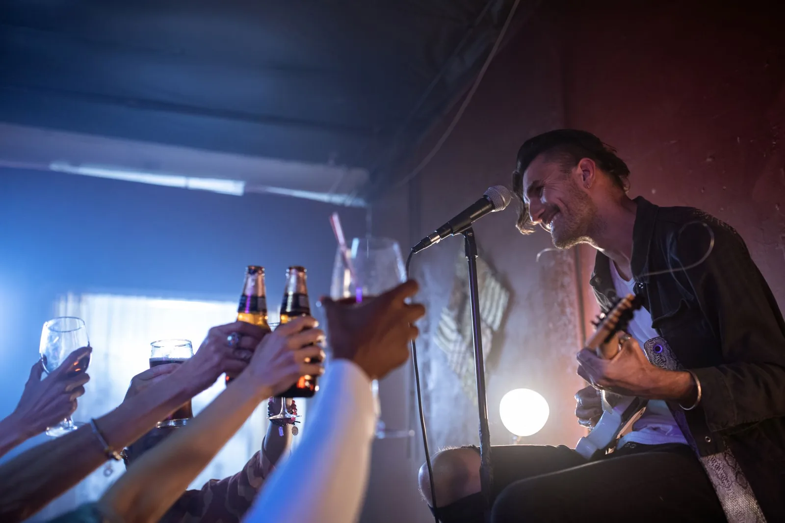 Trubadur synger og spiller guitar til en fest, mens gæsterne skåler med flasker i hånden